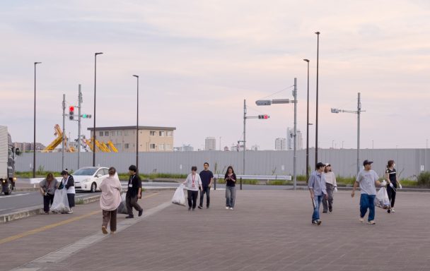 夕暮れの公園をゴミ袋を手に歩く社員たち